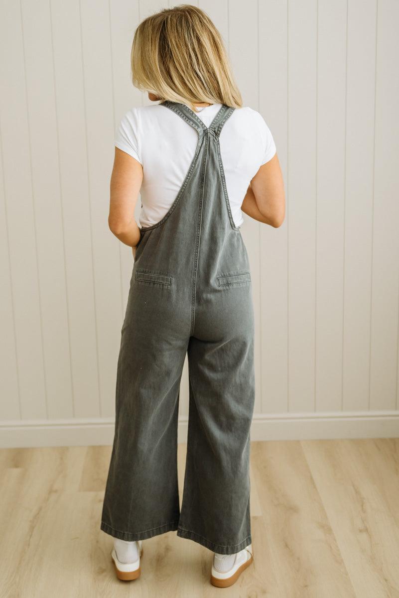 Person wearing gray overalls and a white shirt against a light wooden paneled wall.