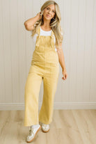 Woman wearing a yellow denim jumpsuit against a white paneled wall.