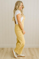 Woman wearing yellow overalls and white shoes against a beige wall.