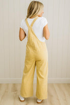 Woman wearing yellow overalls and a white shirt against a light wooden paneled wall.