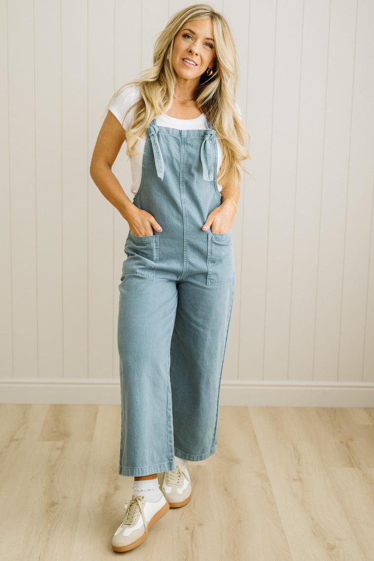 Woman wearing a light blue denim jumpsuit against a white paneled wall.