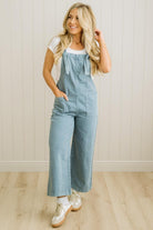 Woman wearing a light blue denim jumpsuit against a white wall.