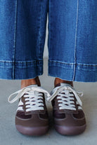 Brown sneakers with white laces worn with blue jeans on a neutral background