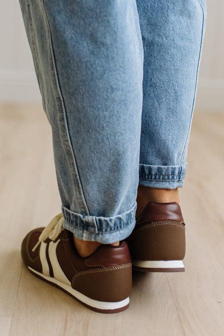 Brown sneakers with white laces worn with leopard jeans on a light wood floor.