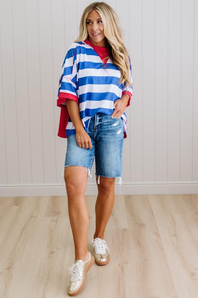 Woman wearing a red, white, and blue striped shirt with denim shorts indoors.
