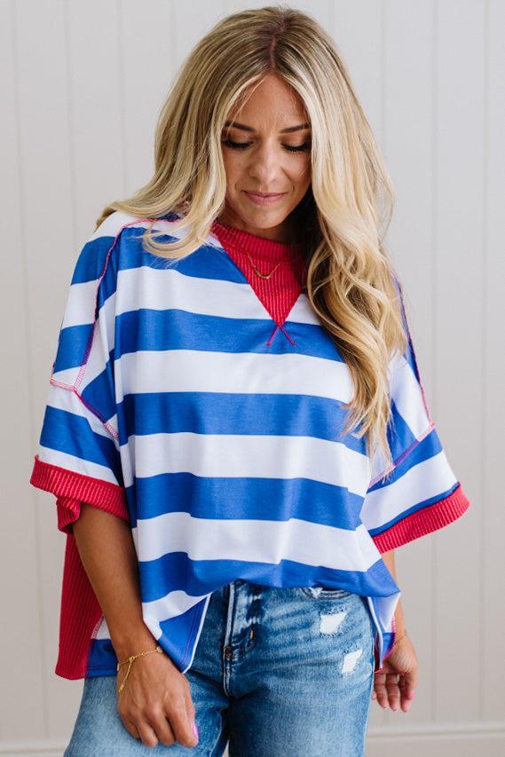Woman wearing a blue and white striped sweater with red accents, standing against a plain background.