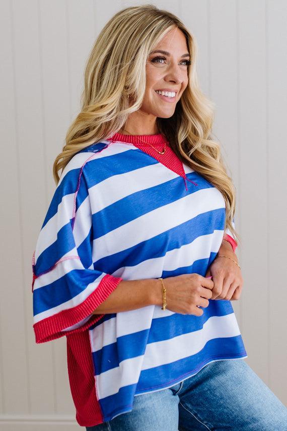 Woman wearing a blue, white, and red striped poncho against a neutral background