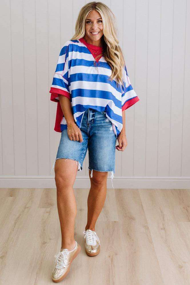 Woman wearing a red, white, and blue striped shirt with denim shorts on a light wooden floor.