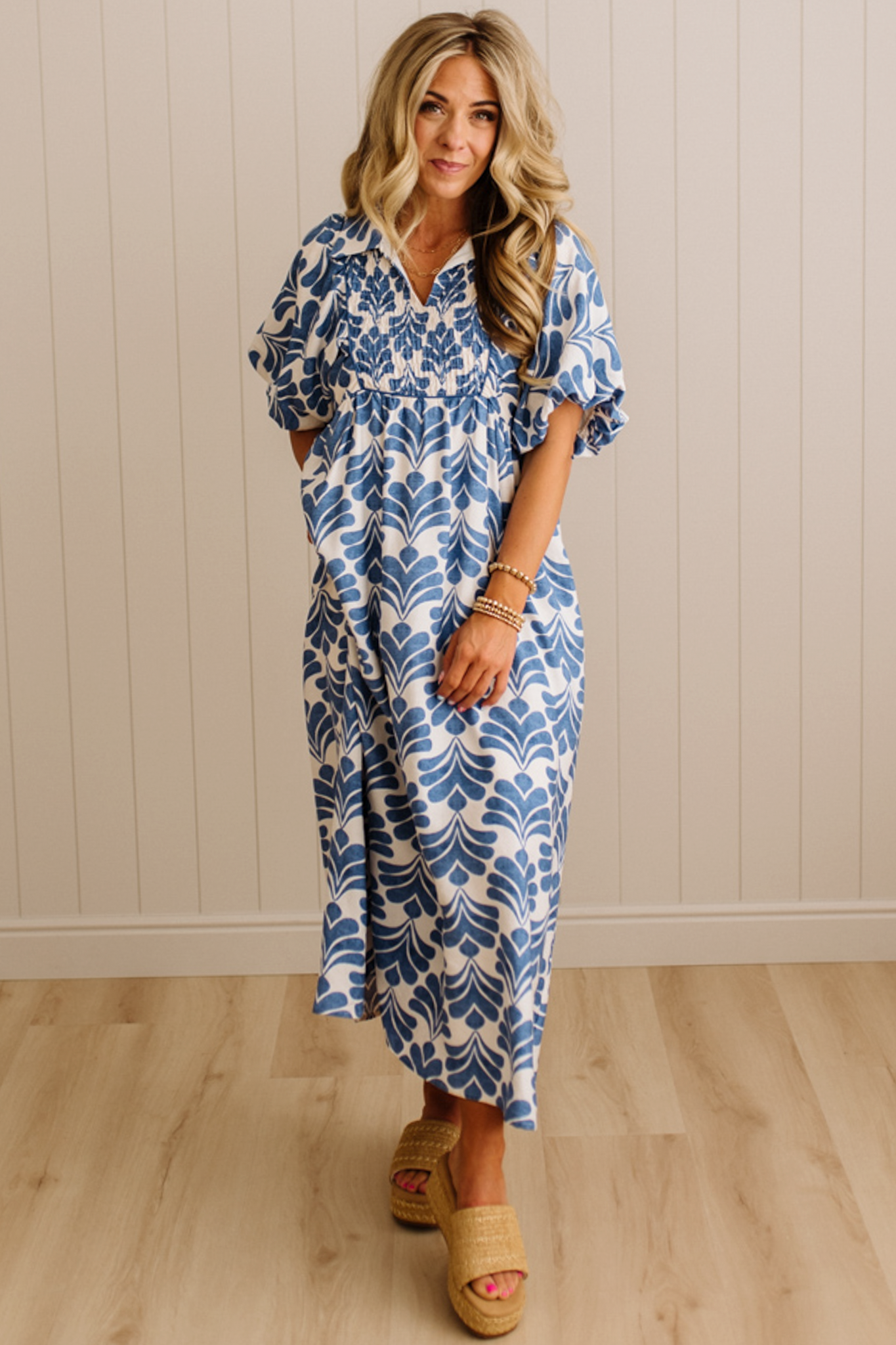 Woman wearing a blue and white patterned dress standing against a beige wall.