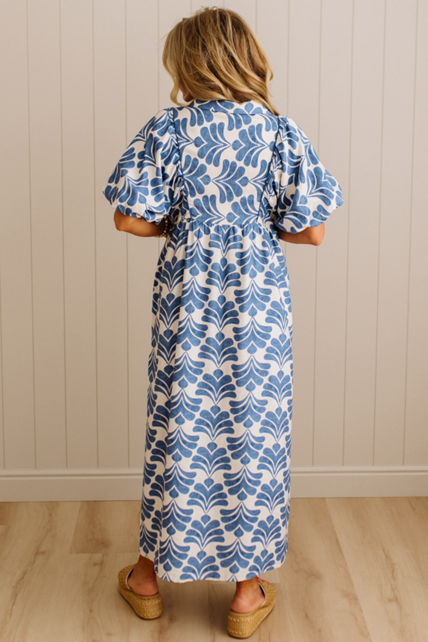 Woman wearing a blue and white patterned dress standing against a beige wall.