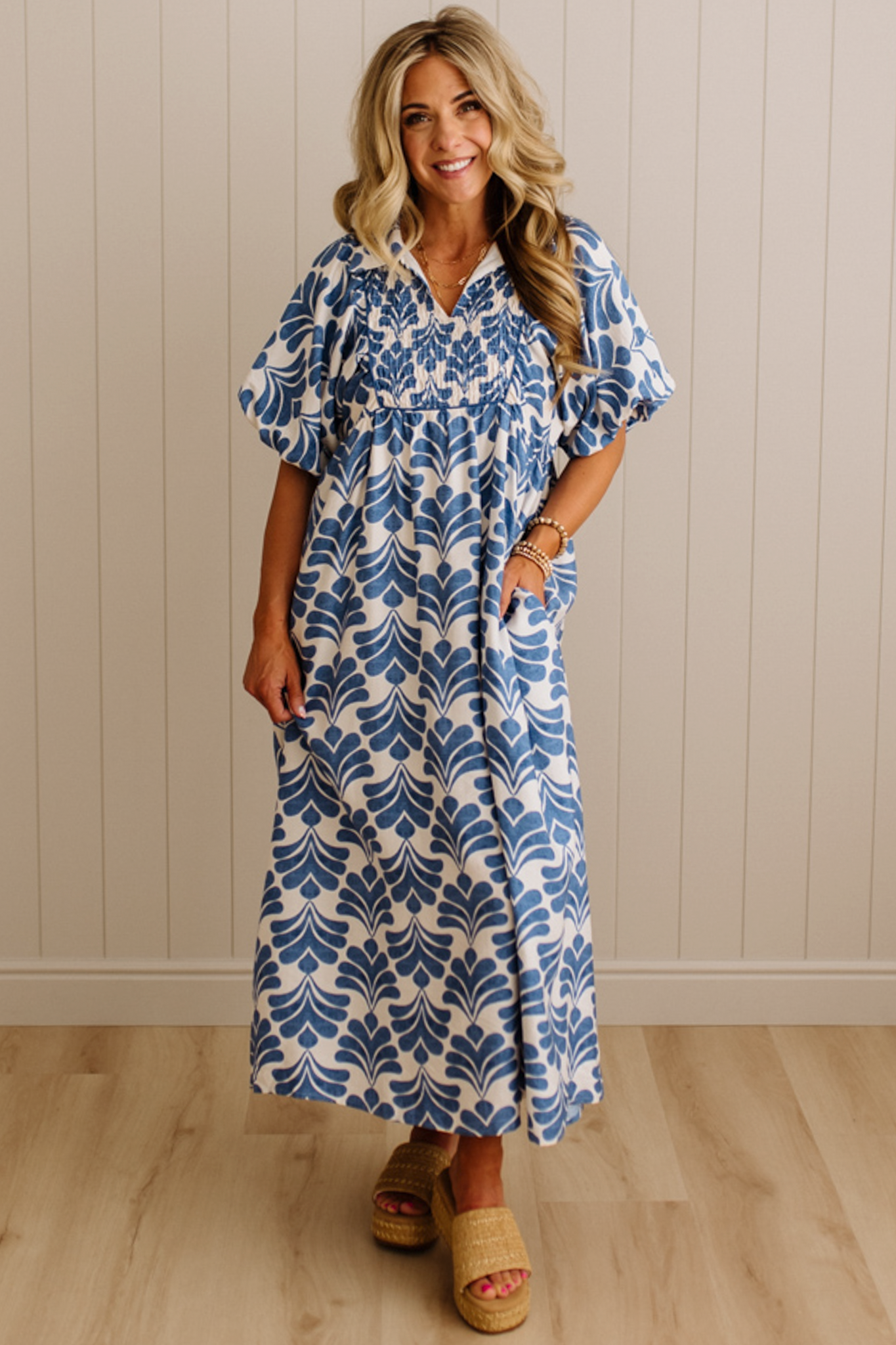 Woman wearing a blue and white patterned dress standing against a beige wall.