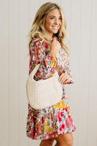 Woman in a floral dress holding a white woven bag against a light wooden panel background