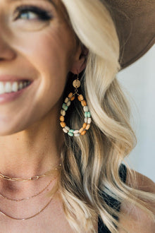  woman wearing a teardrop shaped earring with multi colored wooden beads and gold accents