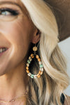 woman wearing a teardrop shaped earring with multi colored wooden beads and gold accents