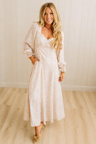 Woman wearing a white floral dress standing in a room with wooden flooring and a white paneled wall.