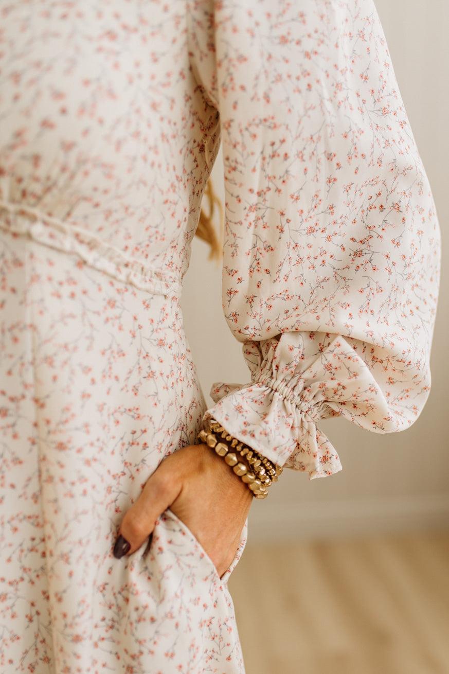 Close-up of a person wearing a floral dress with puffed sleeves, holding their hand in front.