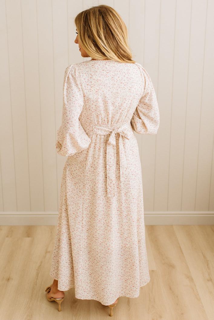 Woman wearing a long, light-colored dress with a subtle pattern against a plain background.