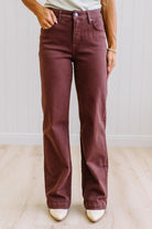 Woman wearing dark brown high rise pants with wide leg cut, on a light wood floor with neutral background.