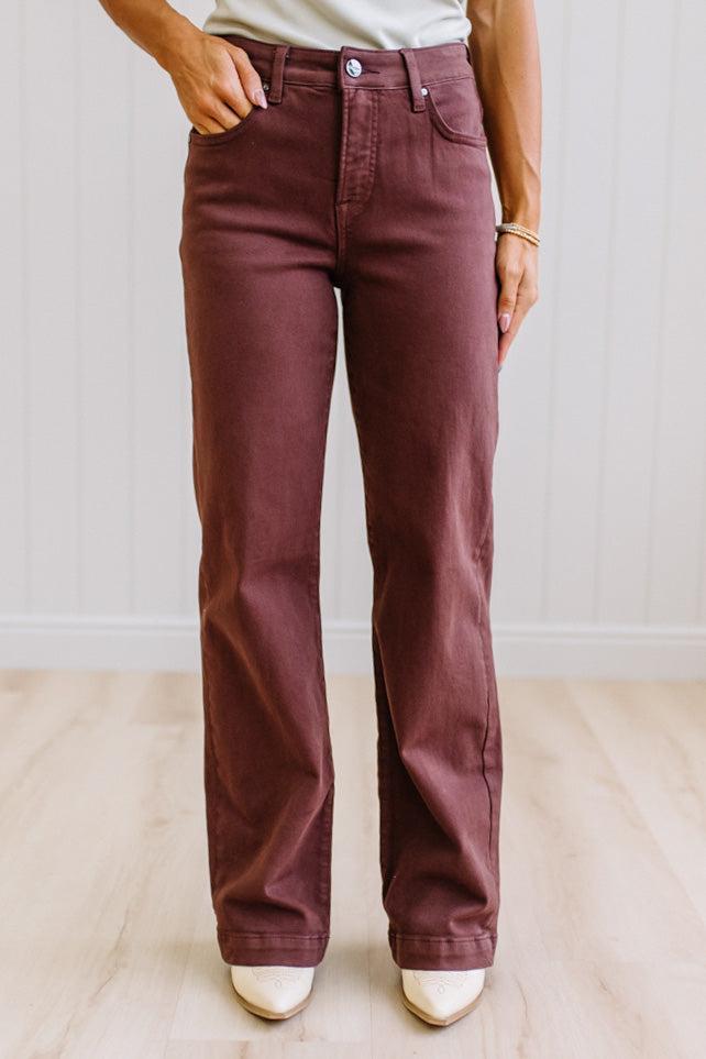 Woman wearing dark brown high rise pants with wide leg cut, on a light wood floor with neutral background.