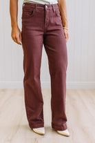 Woman wearing dark brown high rise pants with wide leg cut, on a light wood floor with neutral background.