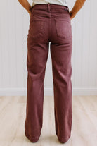 Woman wearing dark brown high rise pants with wide leg cut, on a light wood floor with neutral background.