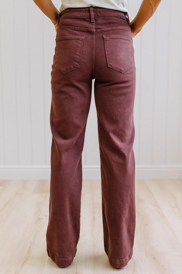 Woman wearing dark brown high rise pants with wide leg cut, on a light wood floor with neutral background.
