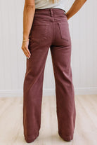 Woman wearing dark brown high rise pants with wide leg cut, on a light wood floor with neutral background.