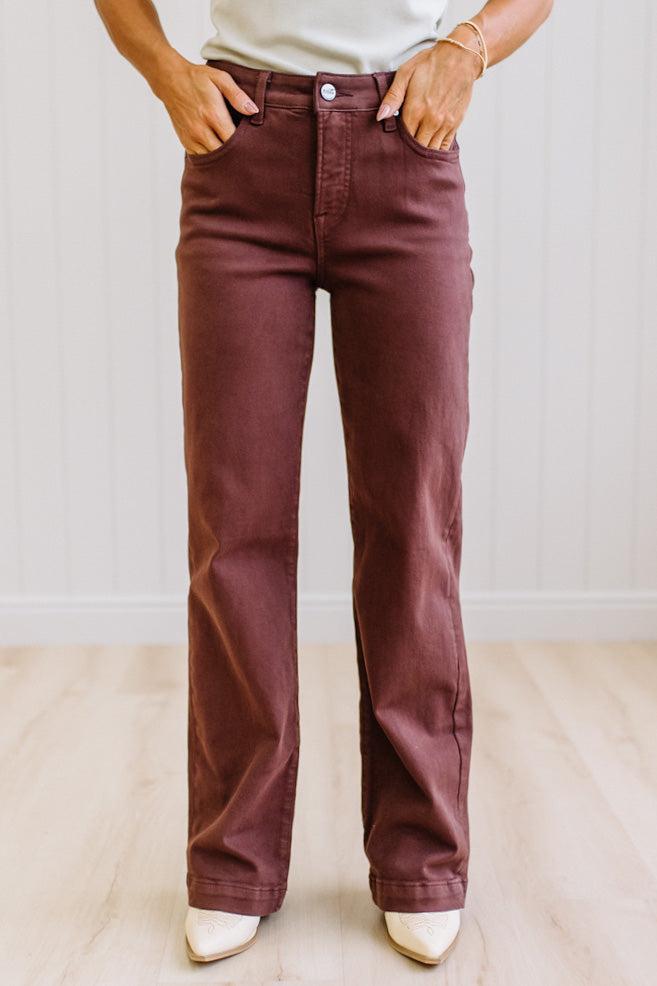 Woman wearing dark brown high rise pants with wide leg cut, on a light wood floor with neutral background.