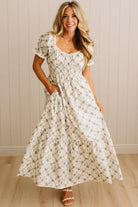 Woman wearing a floral dress standing against a neutral wall.