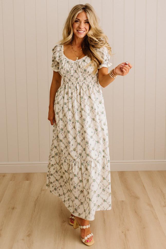 Woman wearing a floral dress standing against a plain wall.