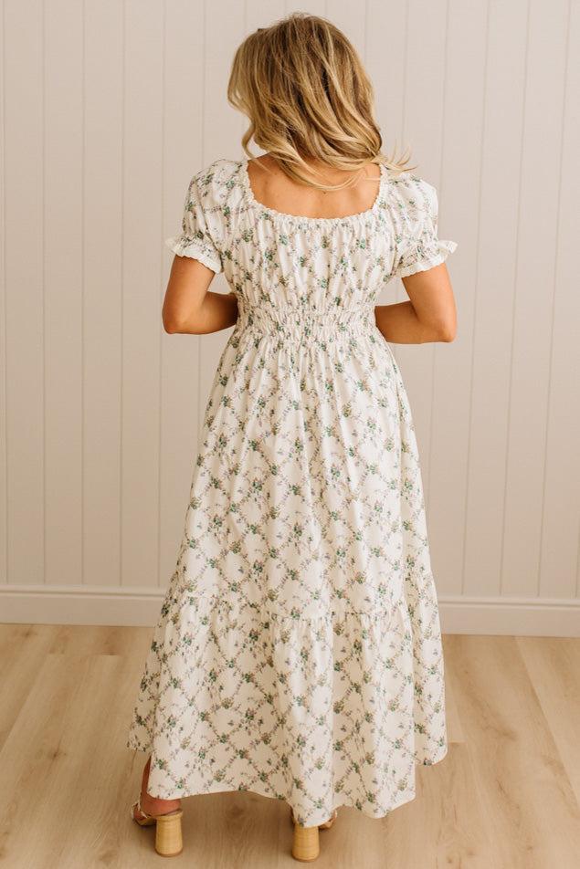 Woman wearing a floral dress standing against a neutral wall.