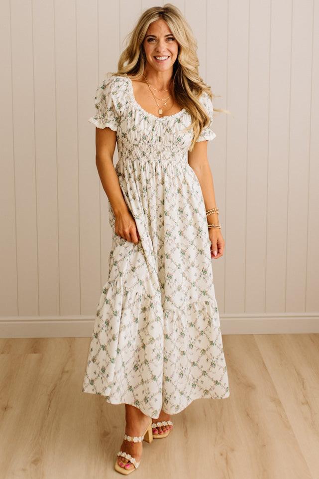 Woman wearing a floral dress standing against a beige wall.