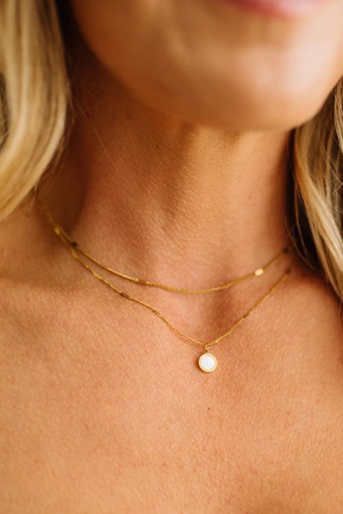 Close-up of a person wearing a delicate gold necklace with a small pendant.