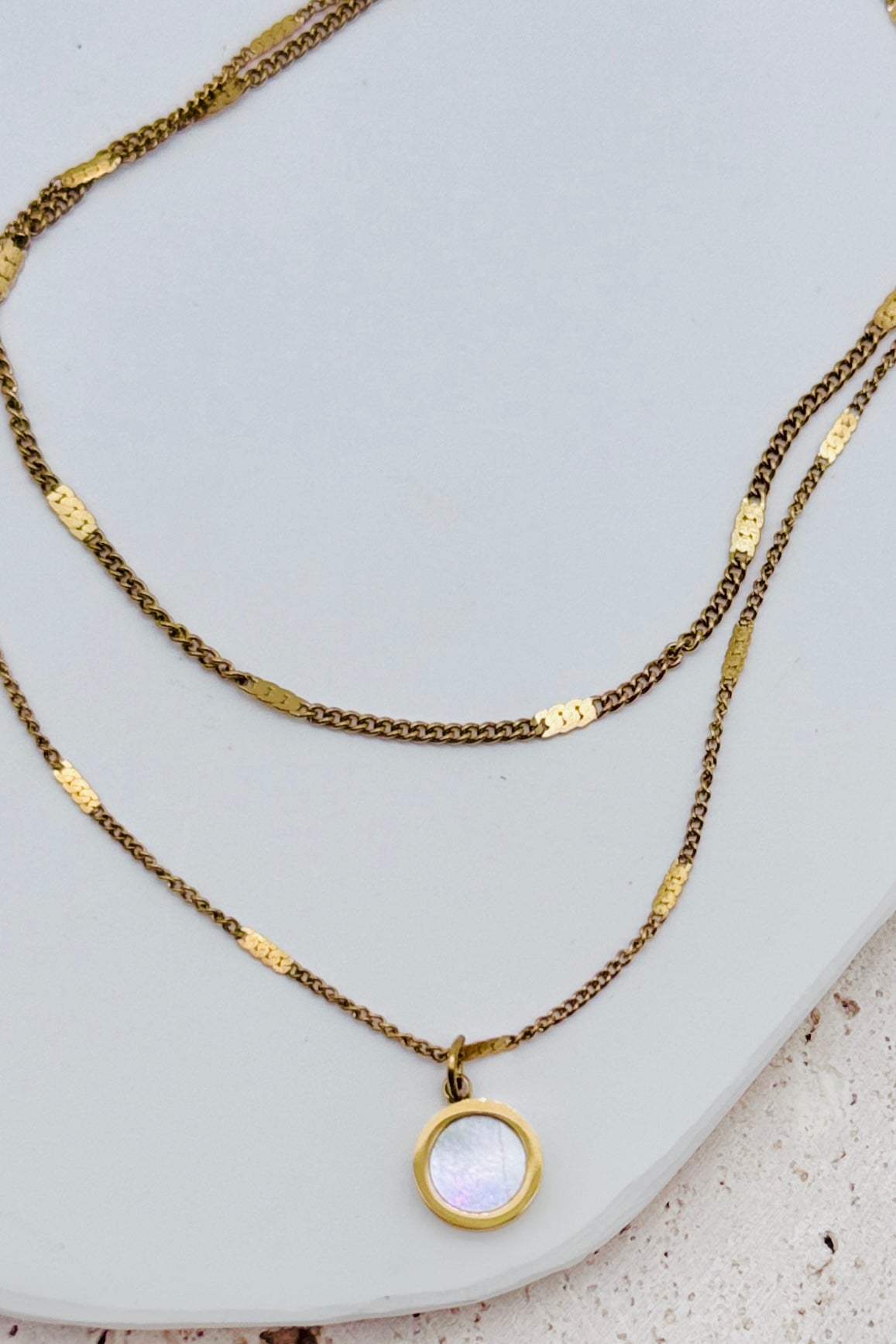 Two gold necklaces with a pendant on a light gray surface