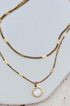 Two gold necklaces with a pendant on a light gray surface