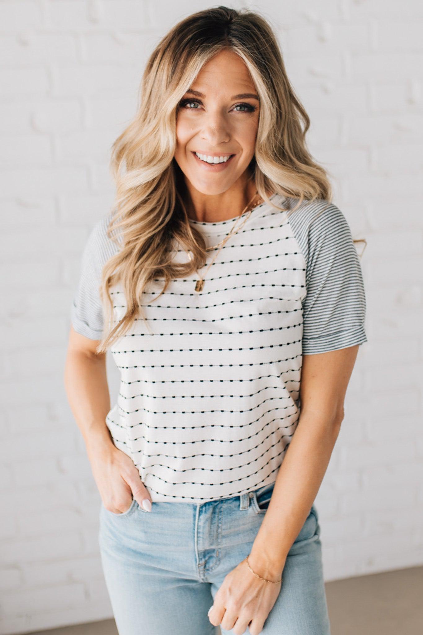 BLONDE WOMAN WEARING A ROUND NECK TOP WITH MICRO STRIPED RAGLAN SHORT SLEEVES, AND DOTTED STRIPE KNIT BODY.