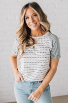 BLONDE WOMAN WEARING A ROUND NECK TOP WITH MICRO STRIPED RAGLAN SHORT SLEEVES, AND DOTTED STRIPE KNIT BODY.