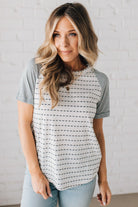 BLONDE WOMAN WEARING A ROUND NECK TOP WITH MICRO STRIPED RAGLAN SHORT SLEEVES, AND DOTTED STRIPE KNIT BODY.