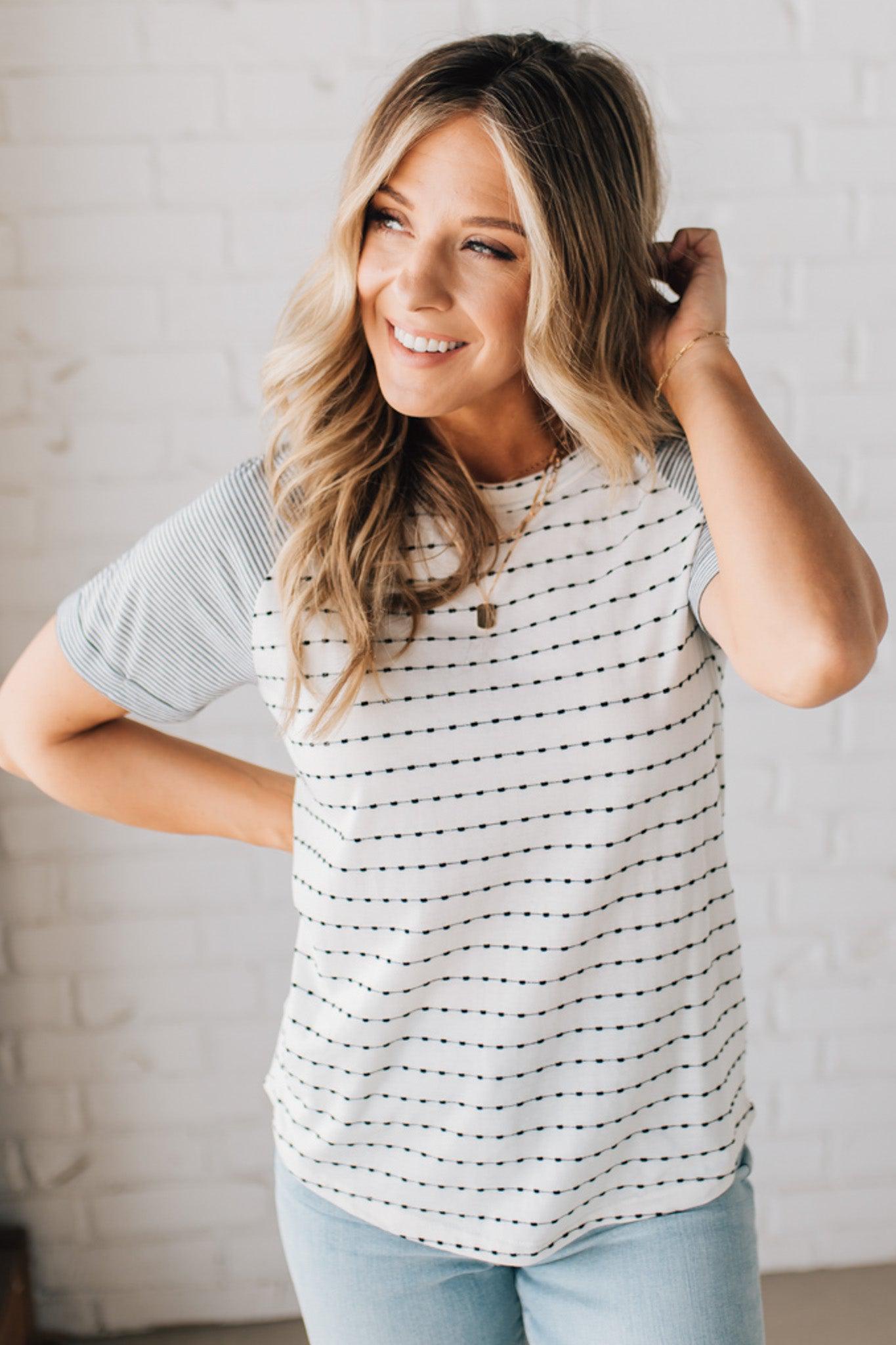 BLONDE WOMAN WEARING A ROUND NECK TOP WITH MICRO STRIPED RAGLAN SHORT SLEEVES, AND DOTTED STRIPE KNIT BODY.