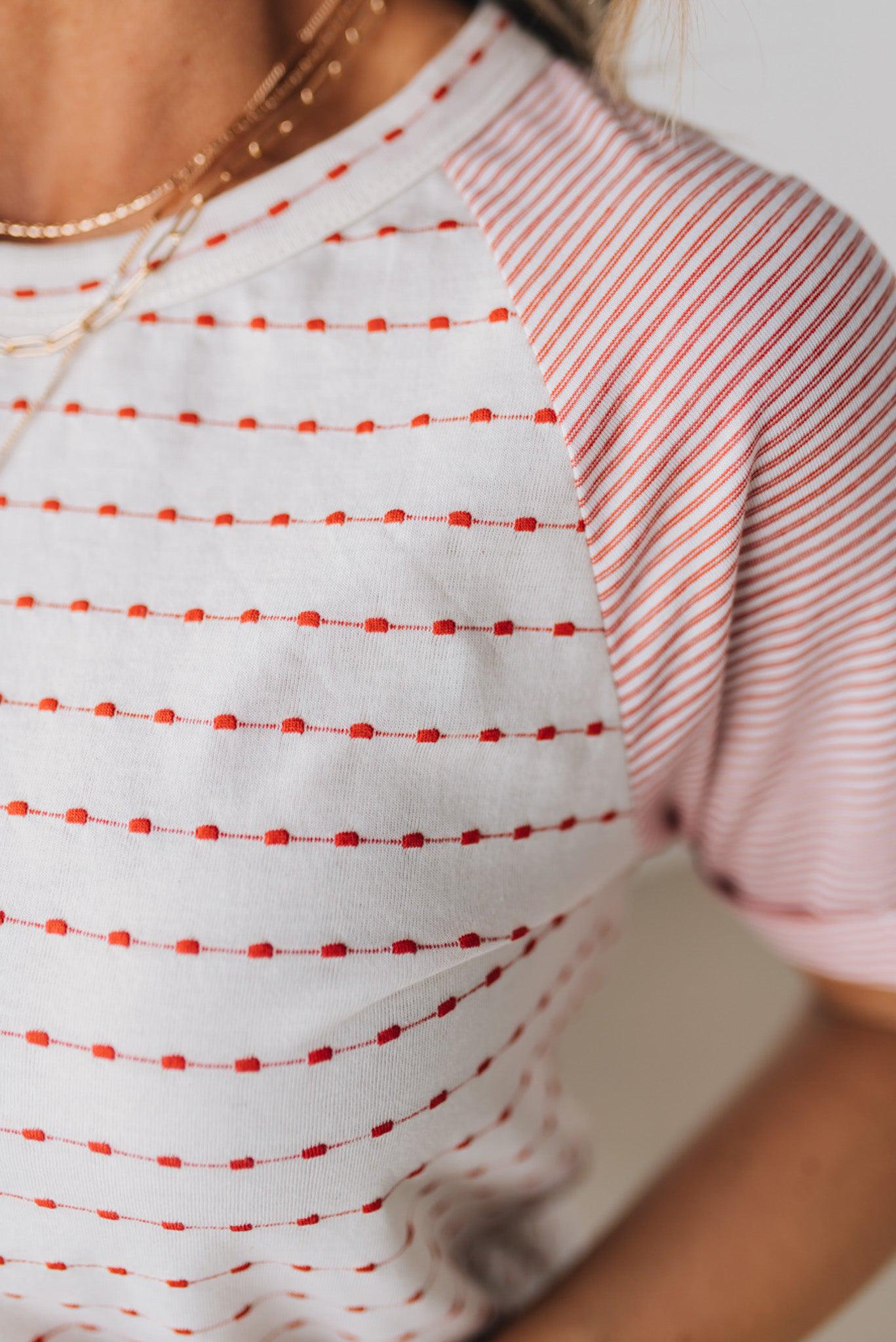 BLONDE WOMAN WEARING A ROUND NECK TOP WITH MICRO STRIPED RAGLAN SHORT SLEEVES, AND DOTTED STRIPE KNIT BODY.