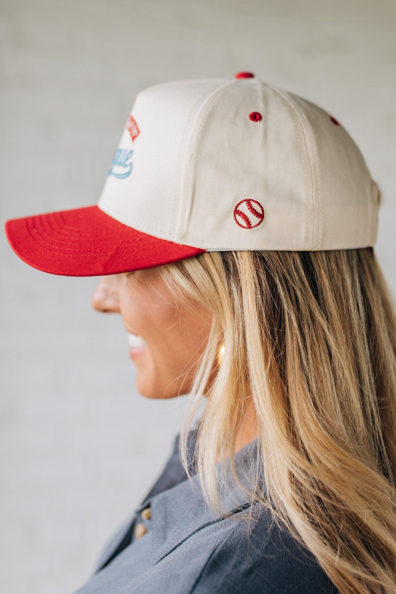 Blonde woman wearing a trucker hat in cream with red brim, and red and blue embroidery at the front "Out of Your League"
