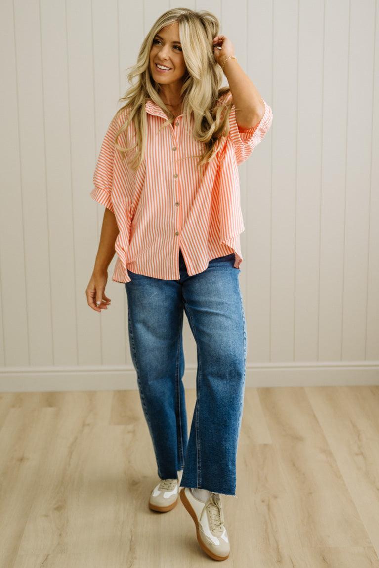 Woman wearing a striped pink shirt and blue jeans indoors.