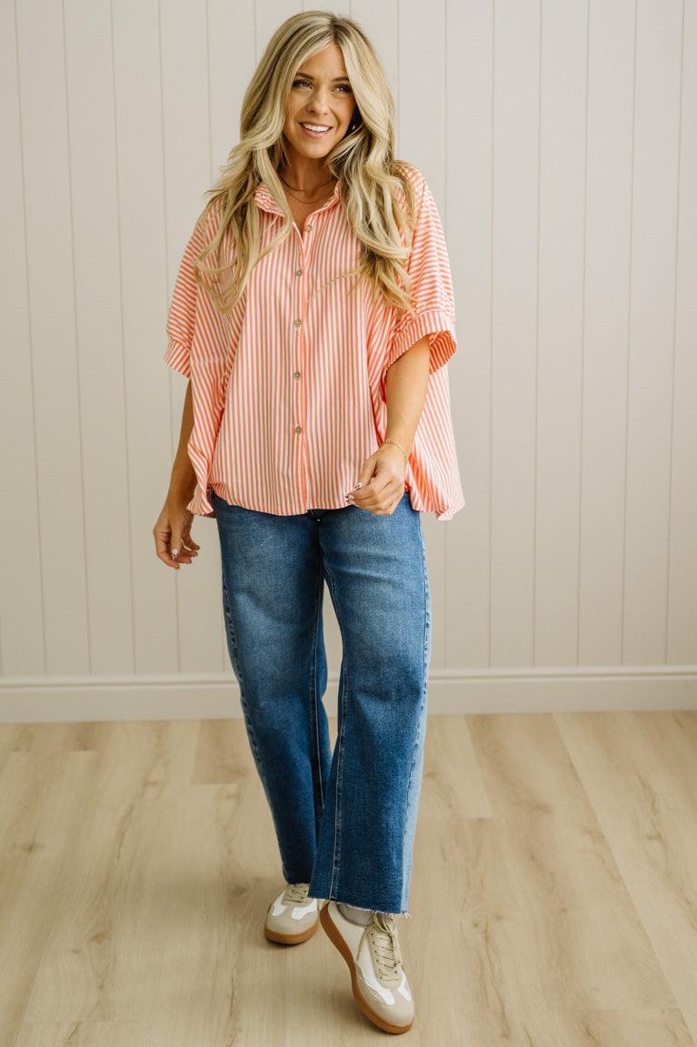 Woman wearing a pink striped shirt and blue jeans standing in a room with wooden flooring and a white wall.