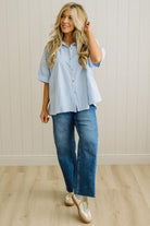 Woman wearing a blue and white striped shirt and jeans standing against a light wooden paneled wall.