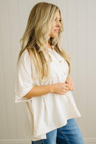 Woman wearing a white textured blouse and blue jeans against a neutral background