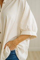 Person wearing a white and beige striped shirt with rolled-up sleeves, standing against a neutral background.
