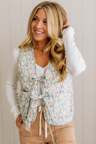 Woman wearing a floral vest over a white long-sleeve shirt with a neutral background