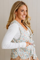 Woman wearing a floral vest over a white shirt against a neutral background