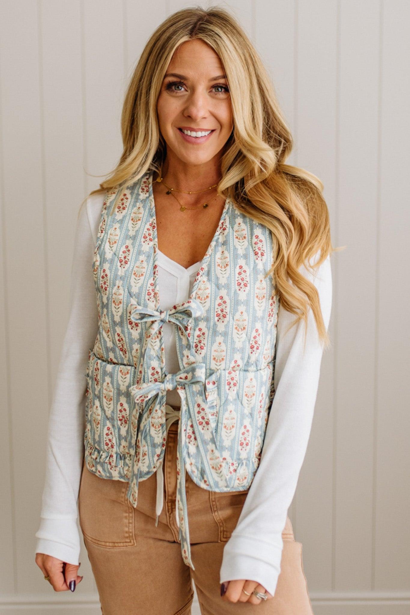 Woman wearing a floral vest over a white shirt with a neutral background