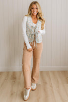 Woman wearing a floral vest, white shirt, tan pants, and white sneakers against a beige wall.